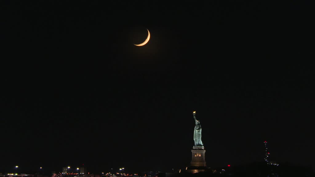 Crescent moon sets behind the Statue of Liberty in NYC